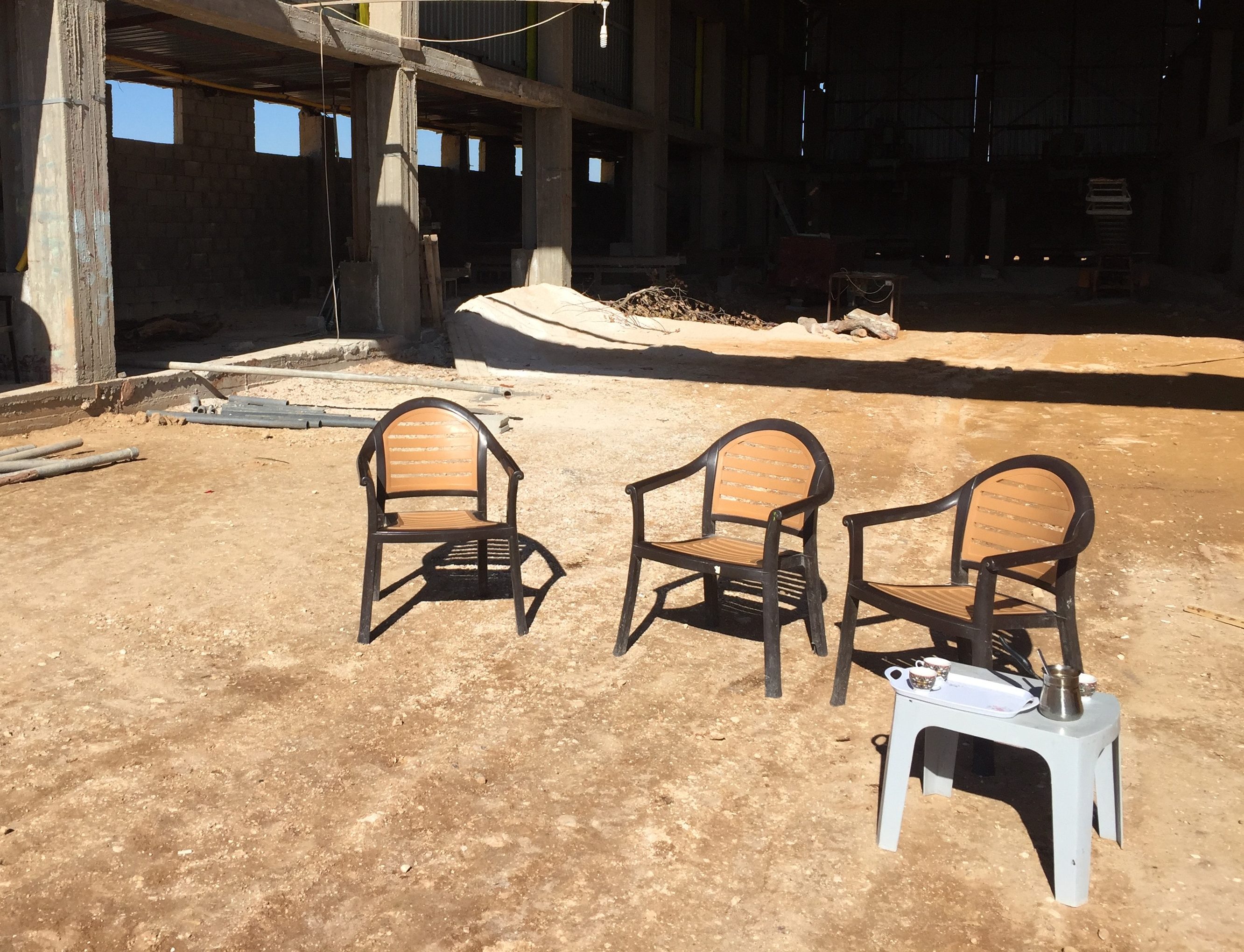 3 empty plastic chairs and a small table with coffee in a construction site